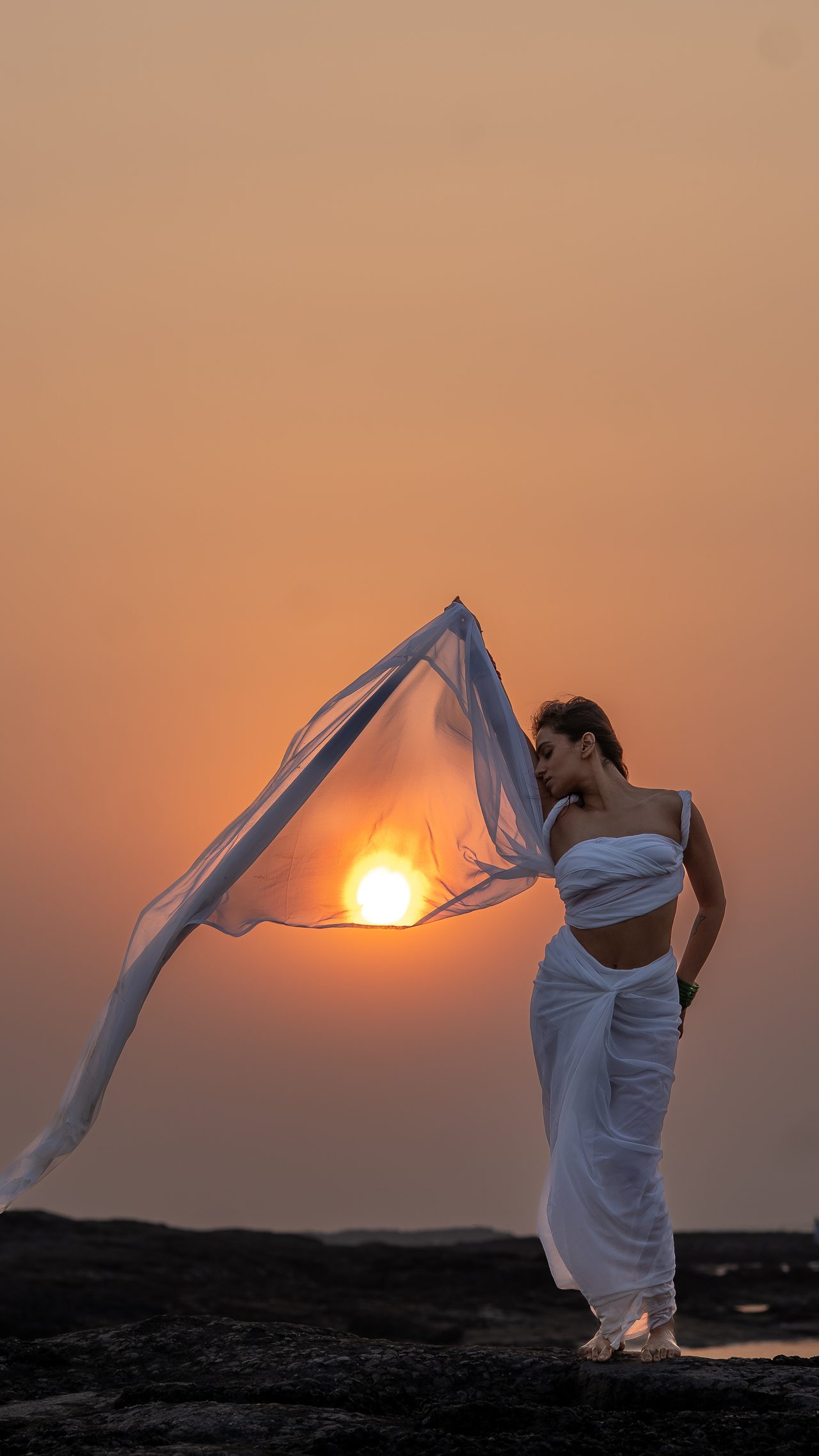 Siffaat Gandhi — white drape lifted against the setting sun, coastal sundown