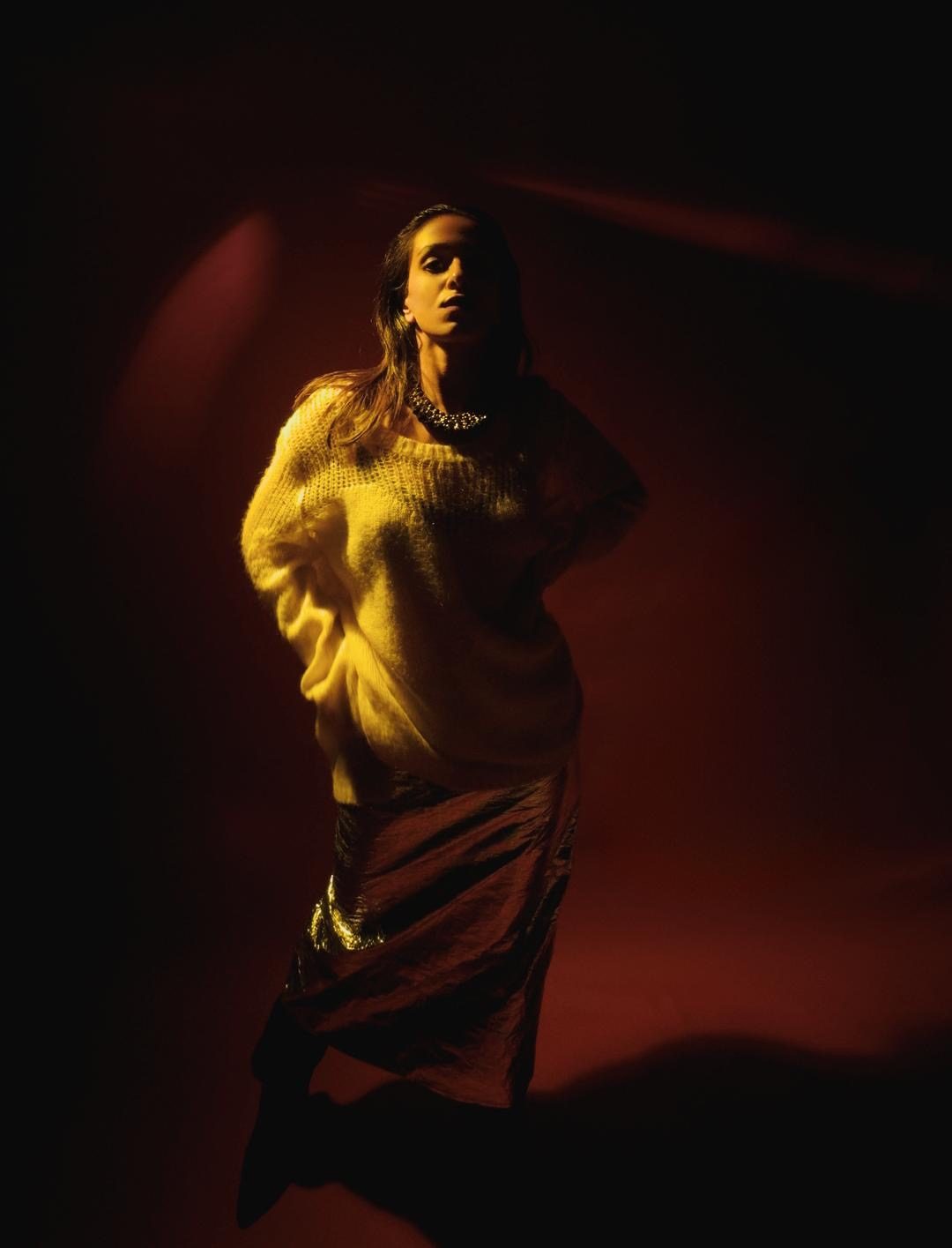 Siffaat Gandhi — dramatic stage light, yellow knit, deep red room
